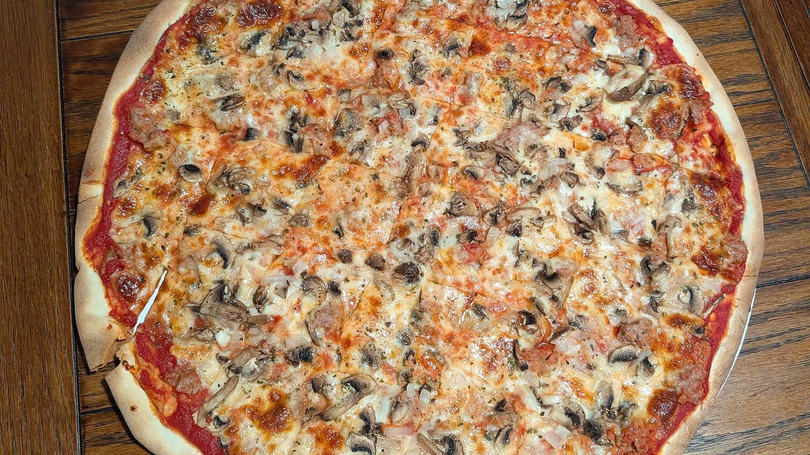A thin-crust Milwaukee-style tavern pizza with mushrooms and sausage on a wooden table