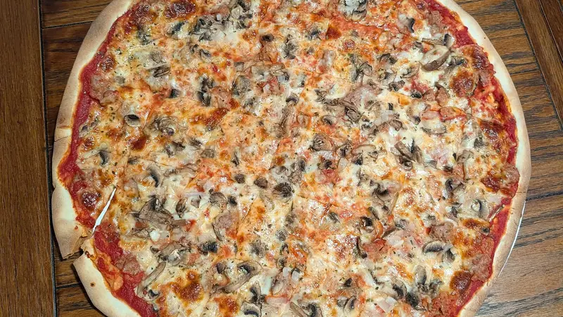 A thin-crust Milwaukee-style tavern pizza with mushrooms and sausage on a wooden table