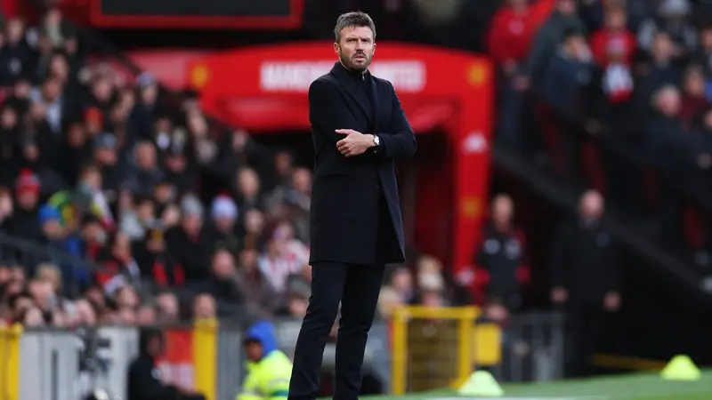 Manchester United manager Michael Carrick in a dark overcoat standing on the touchline at Old Trafford with arms folded