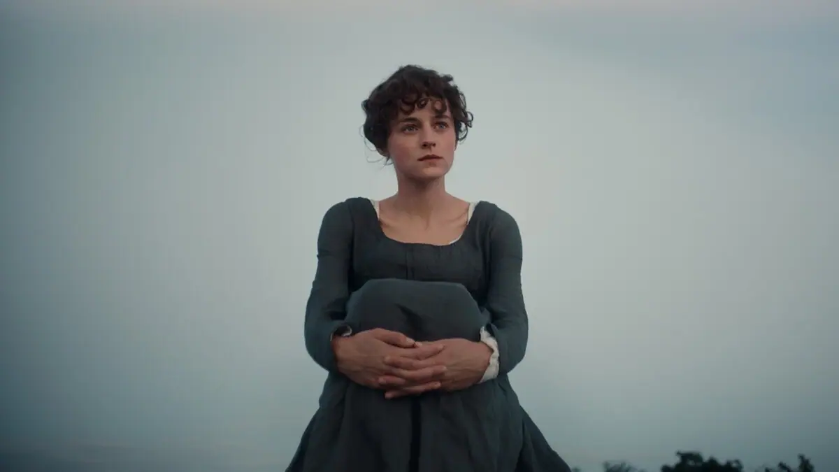 Emma Corrin as Elizabeth Bennet sitting outdoors at dusk in a dark period dress in Netflix's Pride and Prejudice