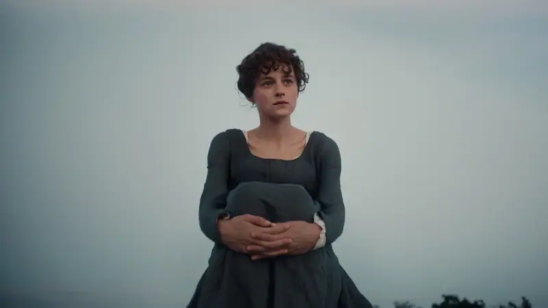 Emma Corrin as Elizabeth Bennet sitting outdoors at dusk in a dark period dress in Netflix's Pride and Prejudice