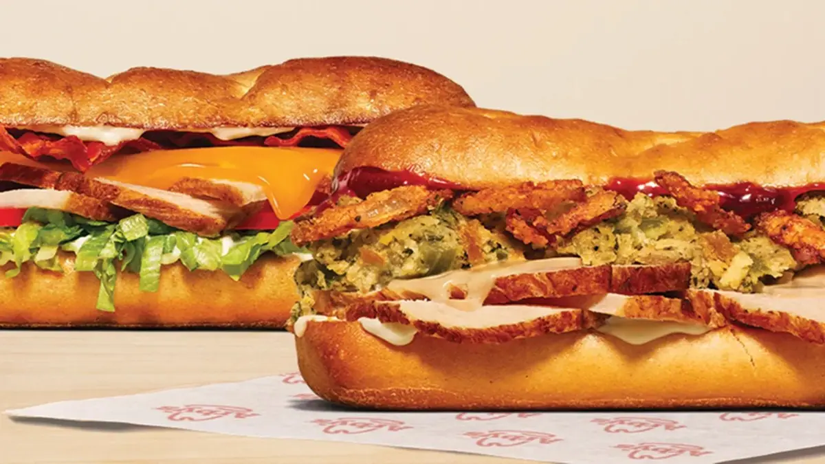 Two Arby's deep fried turkey sandwiches on toasted sub buns, one with bacon and cheddar, the other with stuffing and cranberry spread