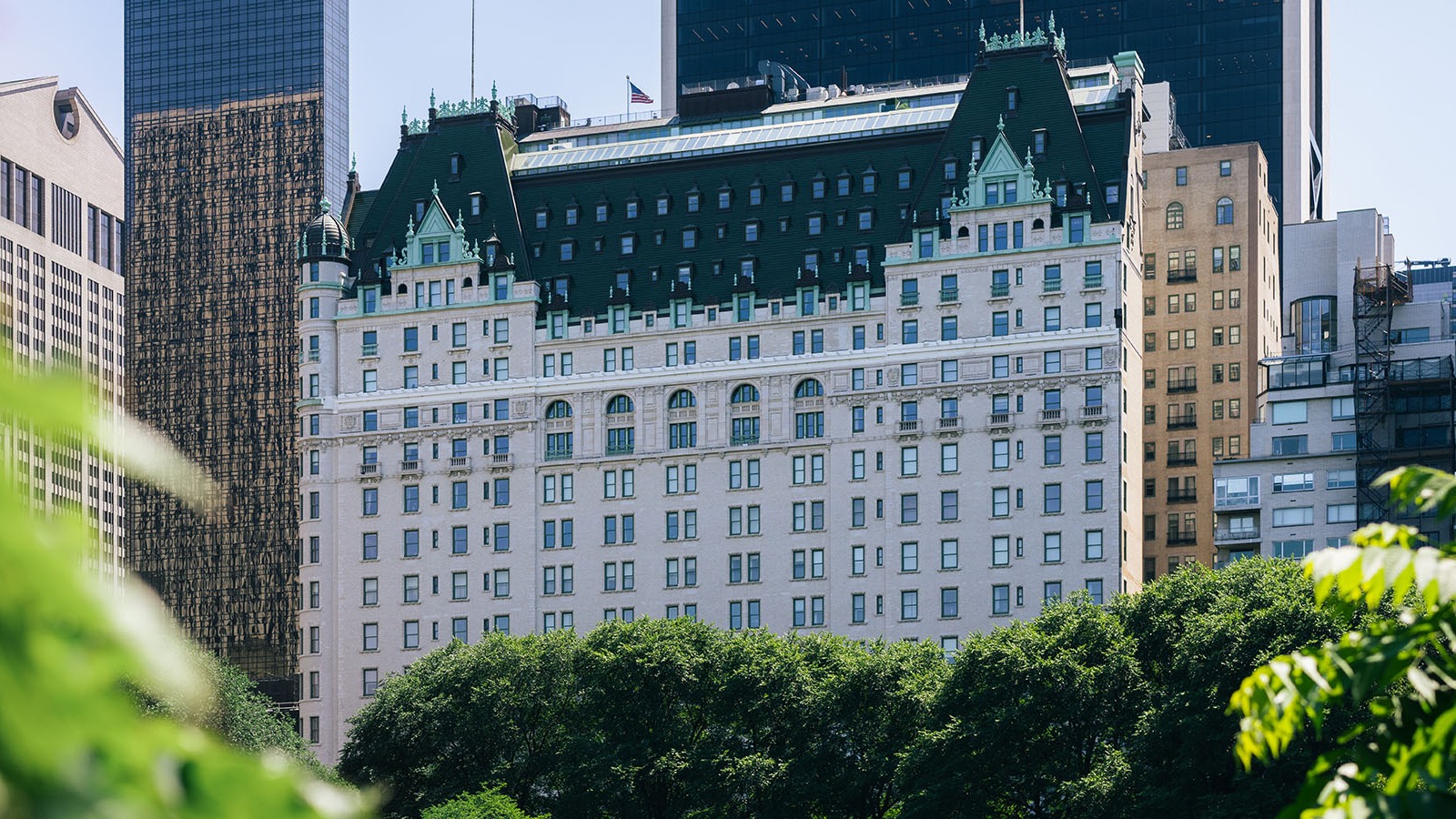 The Plaza Hotel's white marble and green-roofed building on Fifth Avenue seen through trees beside Central Park