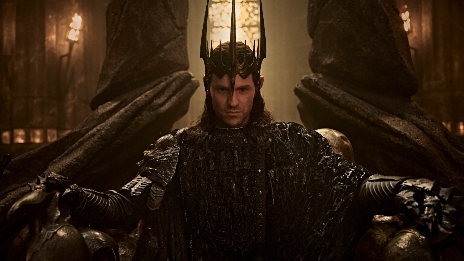 Sauron in a spiked black crown with arms outstretched in a torchlit hall, from The Rings of Power season 3