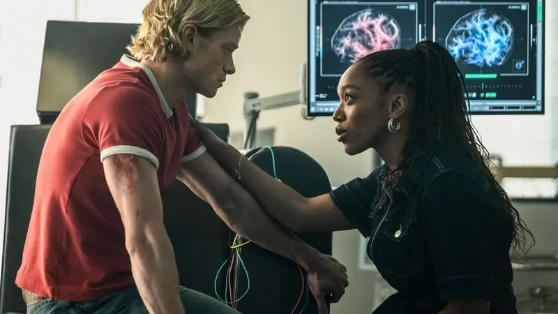 A still from Clayface: a blond man in a red shirt sits beside a woman in a dark denim jacket in front of two brain-scan monitors